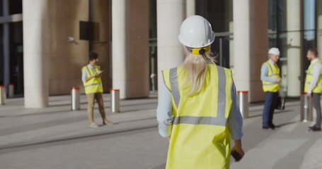 Wall Mural - Back view of female engineer in safety hardhat and vest entering office building