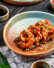 side view of fried shrimps tempura with chopped green onions and sauce on a plate on wooden background