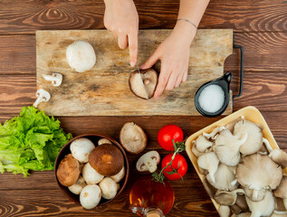 top view of a woman cutting fresh mushrooms on a wooden cutting board and tomatoes with lettuce on rustic wooden background