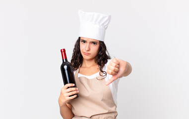 Wall Mural - hispanic pretty chef woman feeling cross,showing thumbs down and holding a wine bottle