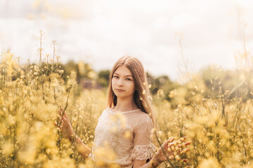 Portrait of a beautiful young girl with long hair against the background of rapeseed flowers. Youth and nature