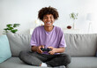 Home entertainments. Happy black teenager with joystick playing online computer games in sofa indoors, full length