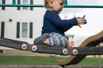 One year old baby taking off shoe at the playground; toddler sits on bouncy bridge 