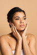 © LIGHTFIELD STUDIOS - pretty african american woman with bare shoulders touching face isolated on beige