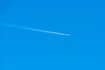 the trace of the plane in the sky. White traces of a jet stream from the combustion of aviation fuel. A passing plane draws white lines on a blue sky without clouds.