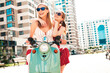 © halayalex - Two young beautiful smiling hipster female in trendy overalls.Sexy carefree women driving retro motorbike on the street background.Positive models having fun, riding classic Italian scooter in eyewear