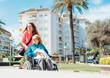 © ADDICTIVE STOCK - Aged mother in wheelchair and adult daughter walking in city