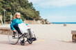 © ADDICTIVE STOCK - Senior woman in wheelchair riding along wooden promenade