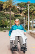 © ADDICTIVE STOCK - Senior woman in wheelchair riding along wooden promenade