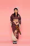 Fototapeta  - Japanese woman with traditional hairdo and kimono holding umbrella on pink background