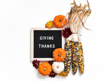 Letter Board With Phrase GIVING THANKS Surrounded By White And Orange Mini Pumpkins And Dried Indian Corn