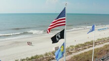 Flags Of USA, POW MIA, Myrtle Beach, Air Force. Aerial Of Atlantic Ocean In South Carolina. Unrecognizable Young African American And Caucasian Men Walk On Beach With Chairs And Cooler.