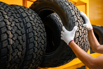 Asian male tire changer Checking the condition of off-road tires in stock so that they can be replaced at a workshop or auto repair shop. Tire warehouse for the car industry