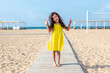 © Inna Tolstorebrova - Adorable curly toddler girl in a yellow dress plays on the white sand beach