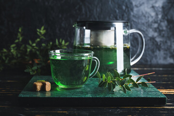 Tea pot and cup of hot green beverage on table