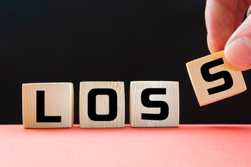 Canvas Print - A businessman holds wooden cubes with a word LOSS on a black background, with space to copy the text, business concept