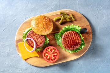 Burgers on a wooden board. Homemade hamburger recipe. Barbecue grilled beef patties with green salad leaves, red onion, tomato etc