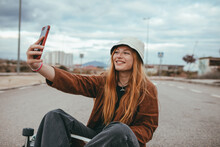 Content Young Lady Sitting On Skateboard And Taking Selfie In Countryside