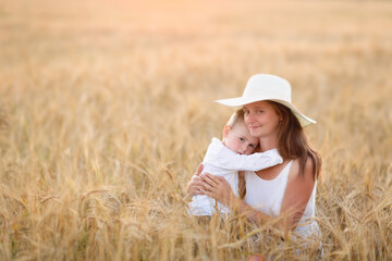 Beautiful American mother and son in a field with wheat, looking at the ears. Summer, organic food and nature