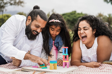 Wall Mural - indian parents having fun at city park playing with wood toys with their daughter - main focus on mo