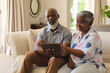 © wavebreak3 - Senior african american couple sitting on sofa using tablet and smiling