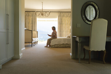 Wall Mural - Senior caucasian woman sitting on bed using smartphone in bedroom