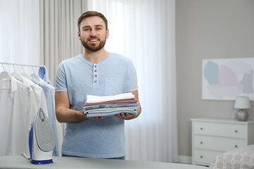 Poster - Man with folded clothes after ironing near board at home. Space for text