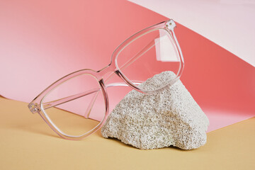 Wall Mural - eye glasses on a concrete podium on a pink and beige background, trend composition, black stylish eye glasses,