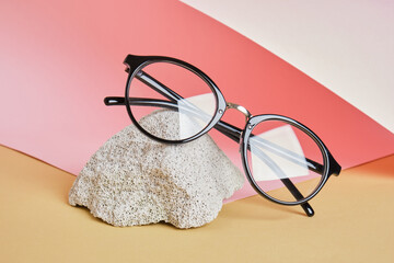 Wall Mural - eye glasses on a concrete podium on a pink and beige background, trend composition, black stylish eye glasses,