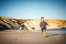 The Small Boy Happily Running On The Beach By Sunset