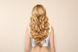 © New Africa - Young woman with long curly hair on beige background, back view