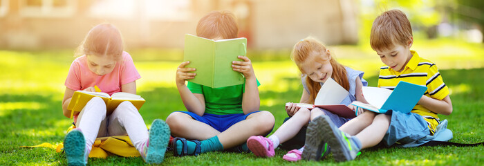 Wall Mural - Children with rucksacks sitting in the park on the grass near the school