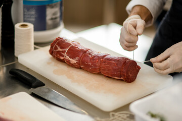 Close-up view of meat and male hands which tie it with butcher's twine