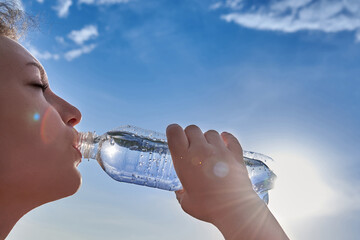  A woman drinks clean transparent water from a plastic bottle.