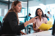 © Wavebreak Media - Two diverse businesswomen sitting at table and using computer with colleagues in background