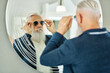 © ADDICTIVE STOCK - Aged man trying on sunglasses in front of mirror in optical store
