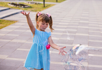 In a public park, a little girl blows and catches soap bubbles.The child is playing and laughing.