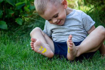 The child was lying on the green grass. Smile with paints on the legs and arms. Child having fun outdoors in the spring park. Selective focus.