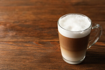 Glass cup of delicious layered coffee on wooden table, space for text