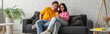 © LIGHTFIELD STUDIOS - positive young couple sitting on couch and looking at cellphone in living room, banner