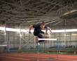 © Cavan Images - Determined male athlete hurdling on stadium