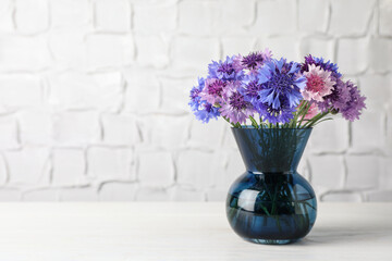 Bouquet of beautiful cornflowers in glass vase on white wooden table. Space for text