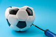 © Victor Moussa - Team sports and competitive athletics concept with deflated football or soccer ball being inflated with a manual pump isolated on blue background