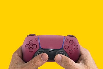 Wall Mural - Male hand holding a Next Generation red game controller isolated on yellow background.
