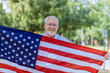 A happy senior patriot wearing a stars and stripes a large American flag.
