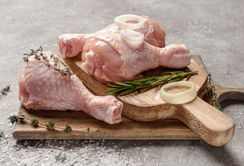 Board with raw chicken legs on grey background