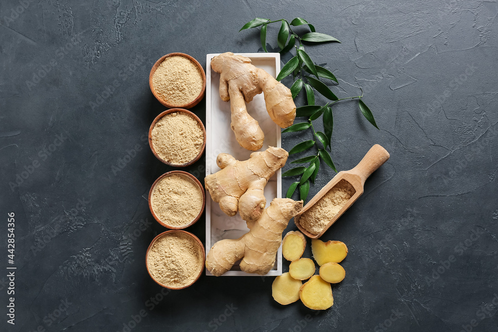 Bowls with ginger powder and roots on dark background