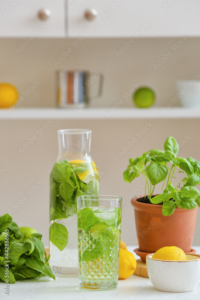 Glass and bottle of lemonade with basil on table in kitchen