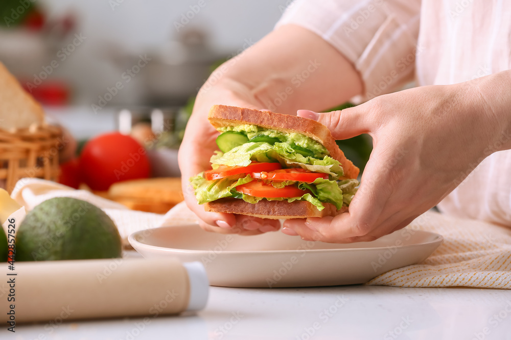 Woman holding tasty sandwich in kitchen, closeup