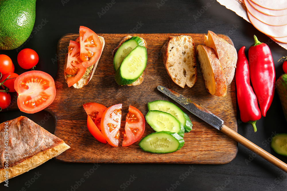 Preparing of tasty sandwiches on dark background